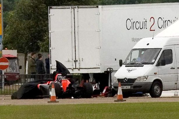 £££ reuse fee applies - Emergency workers and Marussia F1 staff gather around the F1 car still wedged under the lorry with which it collided-1130540
